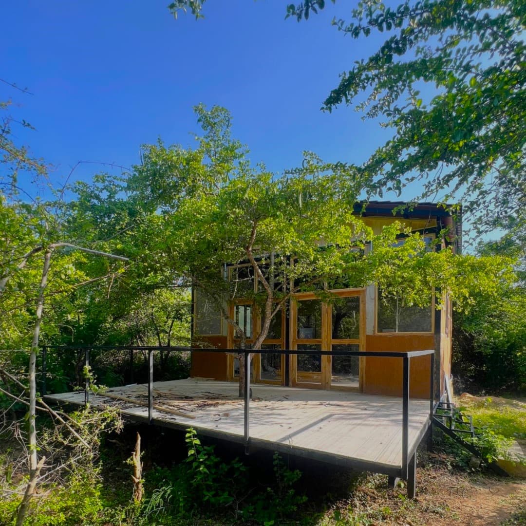 A timber and glass villa raised on stilts among the trees, with a wide open deck across the front