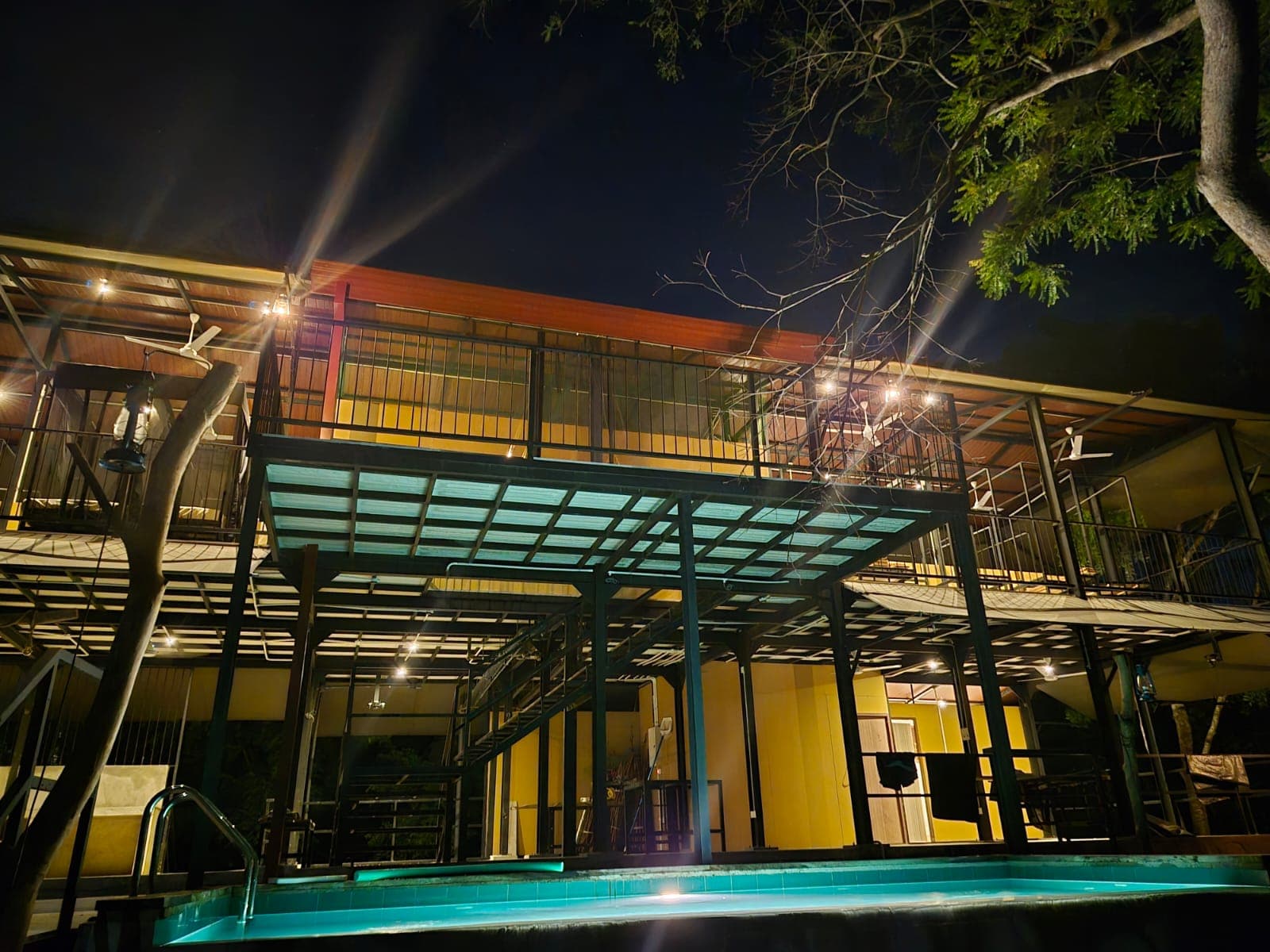 The two-storey hostel lit up at night, with the pool glowing teal in front of it
