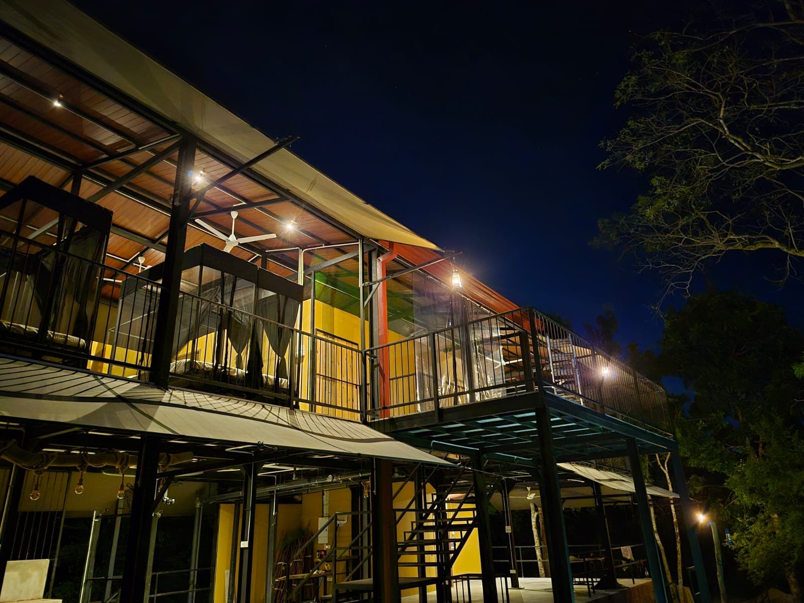 The hostel at night, steel frame and glass, warm light along both floors