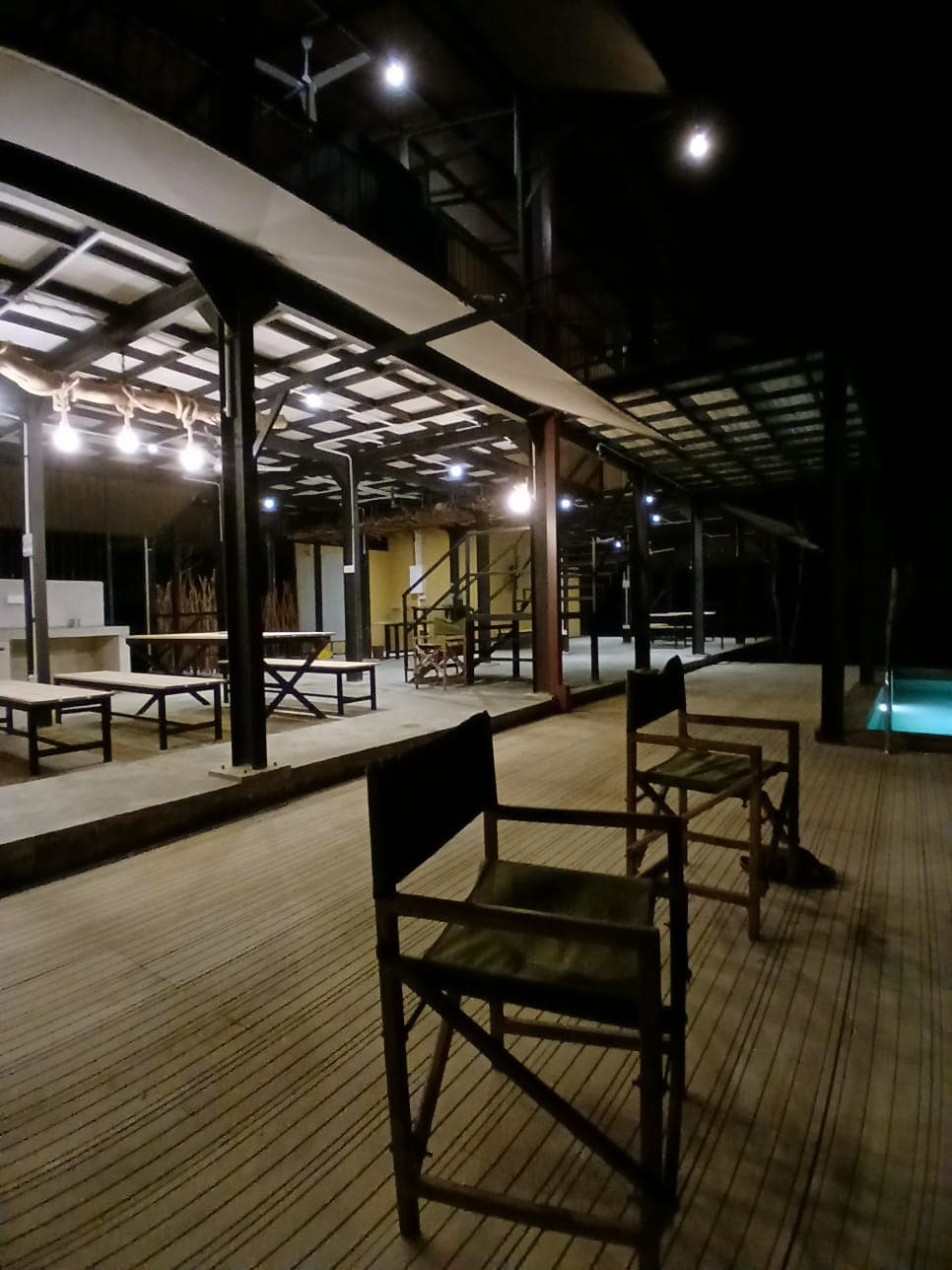 Directors chairs in the foreground of the lit covered deck at night, tables and the pool visible further along