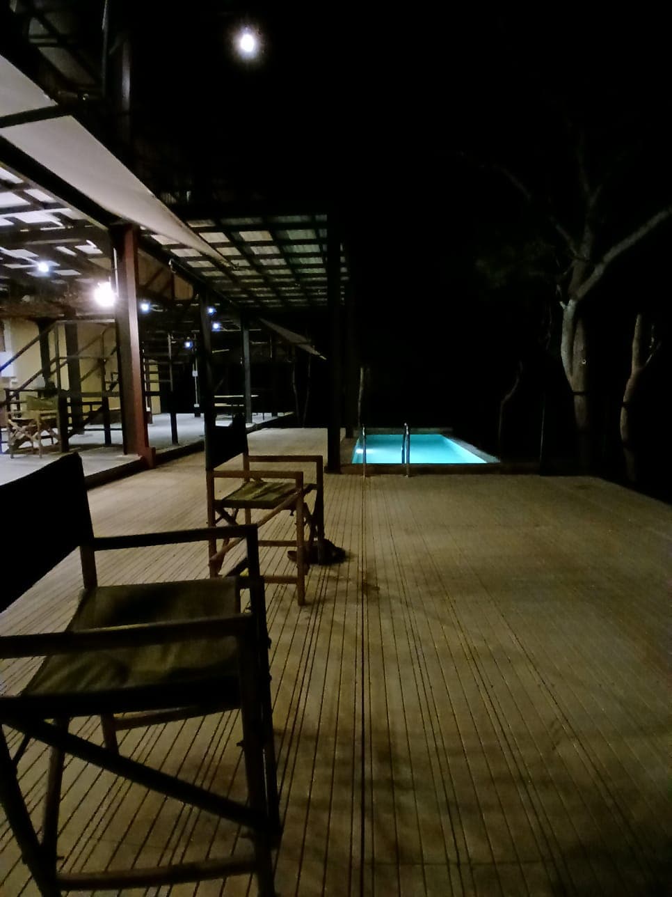 Directors chairs on the deck at night, the pool glowing teal in the middle distance