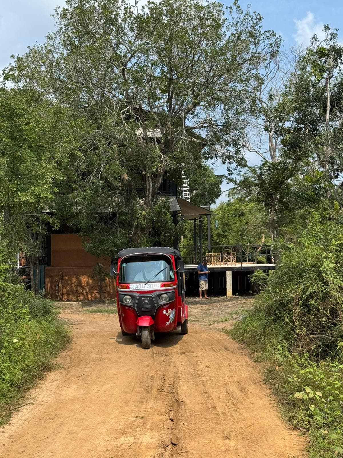 A red tuk-tuk parked on a dirt track running between trees