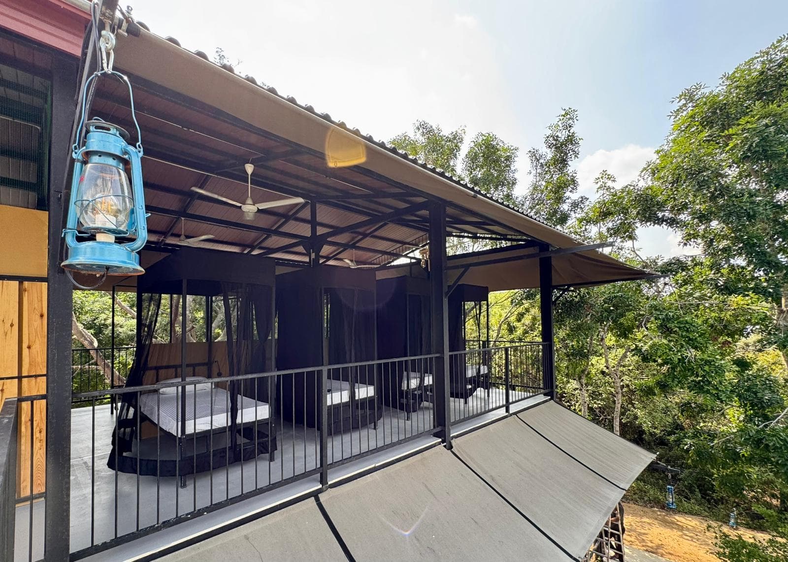 An open room with a made bed, a ceiling fan and a hanging lantern, looking straight out over the deck into the canopy